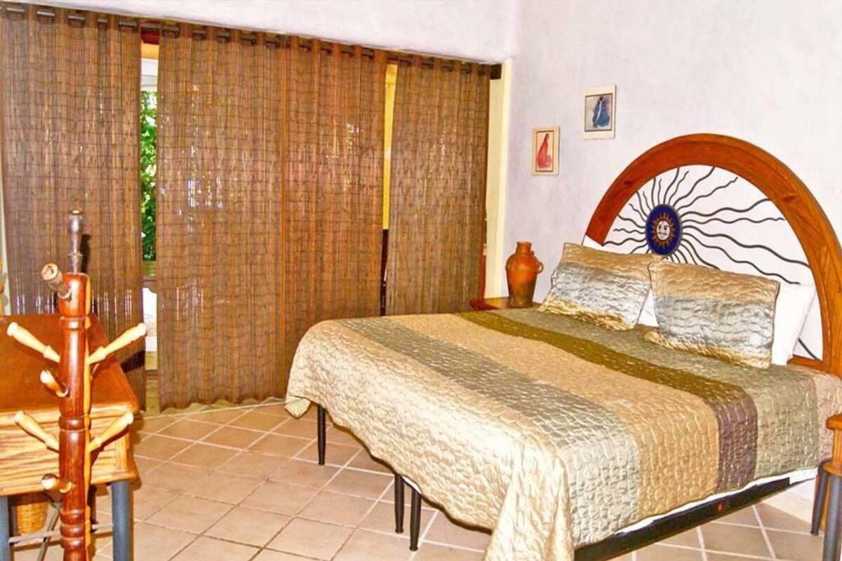 Ein Schlafzimmer mit einem Bett, Vorhängen, einem hölzernen Kopfteil, einem kleinen Tisch und einem Stuhl.