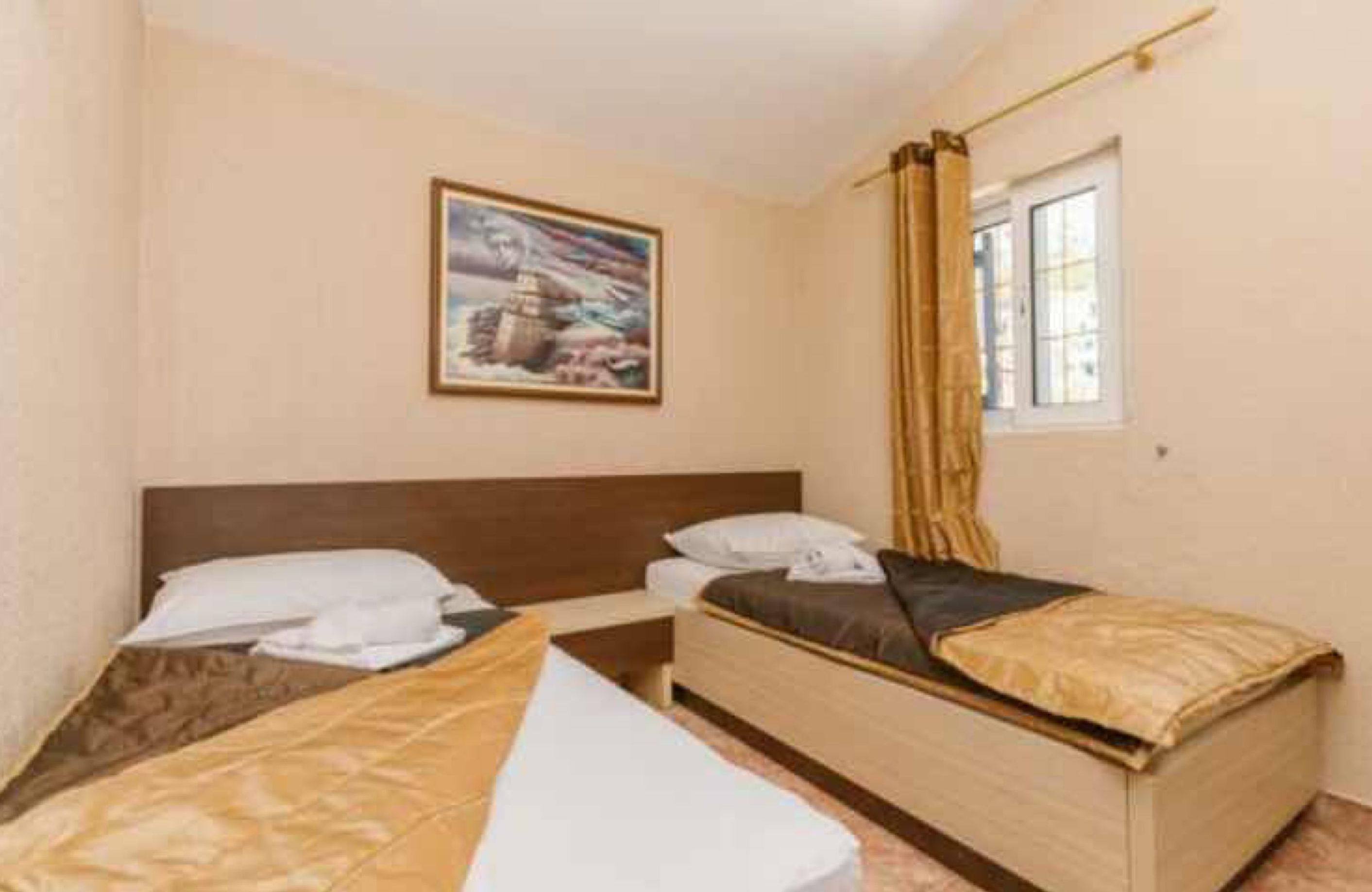 A hotel room with two single beds, a nightstand, a window with curtains, and a painting on the wall.