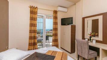 A hotel room with a bed, a desk, a chair, a television, a wardrobe, and a balcony with a view.