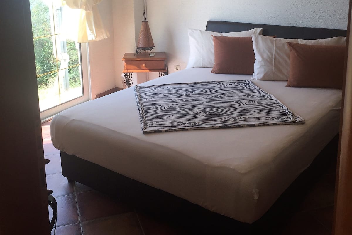 Quarto com cama, mesa de cabeceira, ar condicionado e janela com cortinas.
