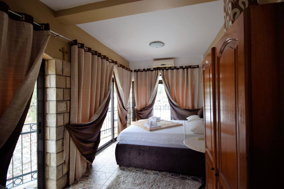 Quarto com uma cama grande, cortinas, guarda-roupa e parede de pedra.