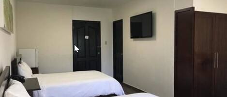 A hotel room with two beds, a wardrobe, a TV, and a door.