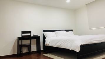 A bedroom with a black bed, white bedding, a wooden chair, and a small desk with a phone.