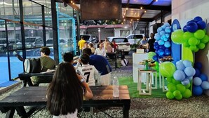 Un área de estar al aire libre con mesas, bancos, una pantalla grande y una decoración con globos.
