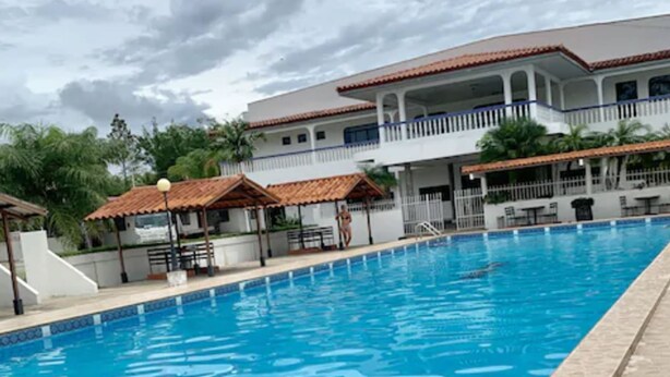 Una piscina con solárium empedrado, un área de estar cubierta y un edificio de varios pisos con balcones al fondo.