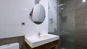 Un baño moderno con un lavabo blanco, tocador de madera, un espejo redondo y una cabina de ducha con paredes de vidrio.