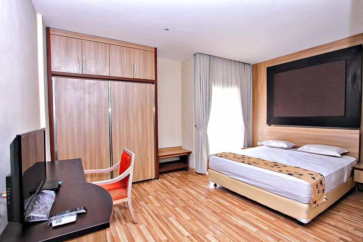 Hotellihuone, jossa on sänky, työpöytä tuolilla, vaatekaappi ja televisio.