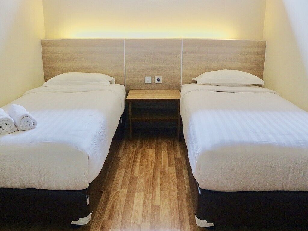 Une chambre d’hôtel avec deux lits simples, des têtes de lit en bois, une table de chevet et un plancher en bois.
