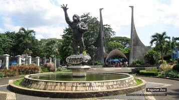 A statue of a person with raised arms, a large abstract sculpture, and a circular water feature in a park setting.