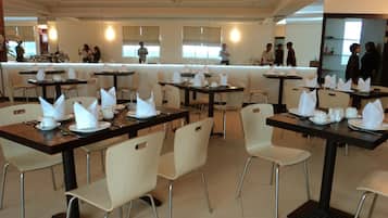 Restaurante moderno com mesas e cadeiras bem organizadas, interior limpo e iluminado, e grandes janelas que permitem a entrada de luz natural.