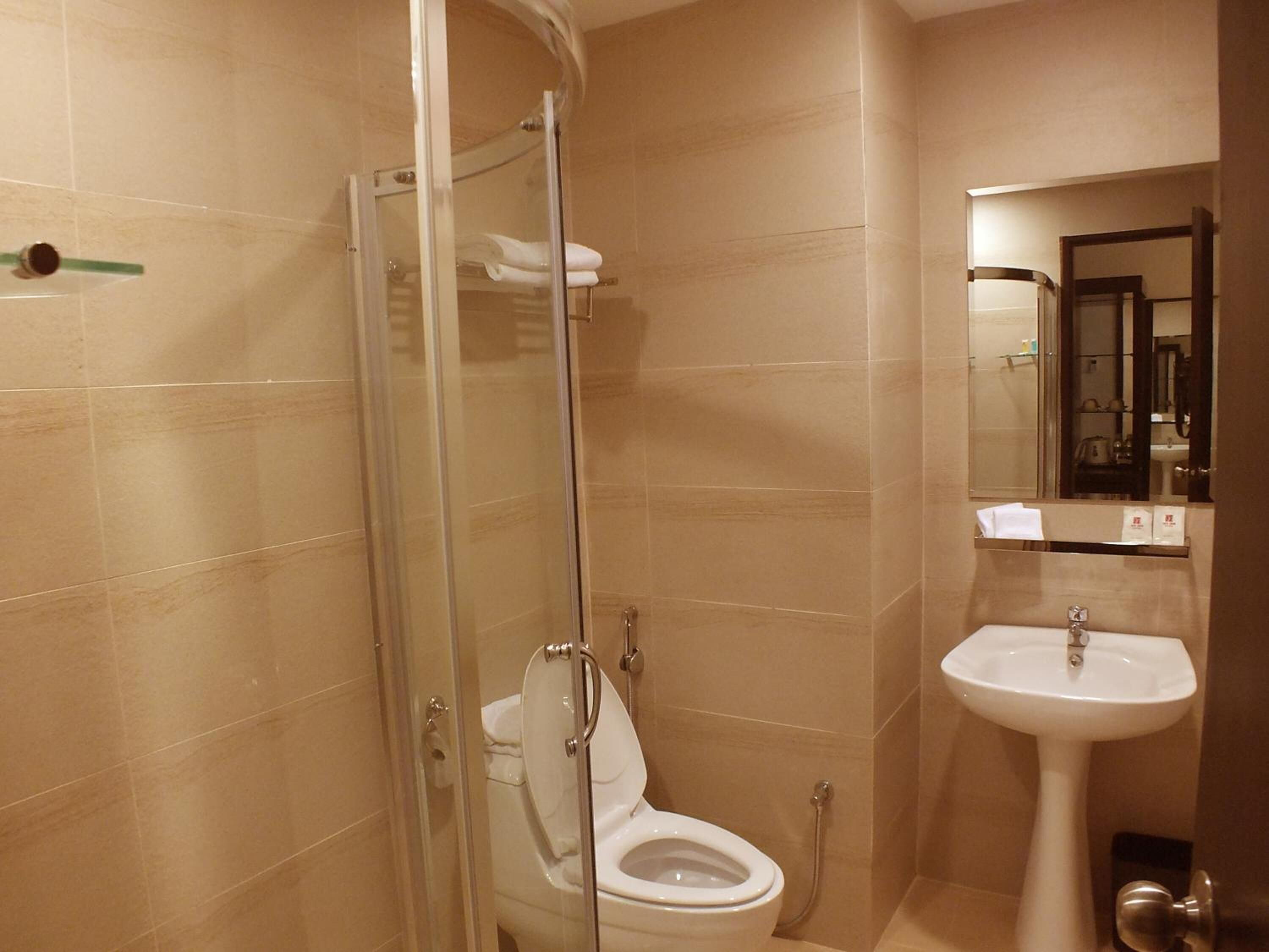 A bathroom with a glass-enclosed shower, a toilet, and a sink with a mirror above it.