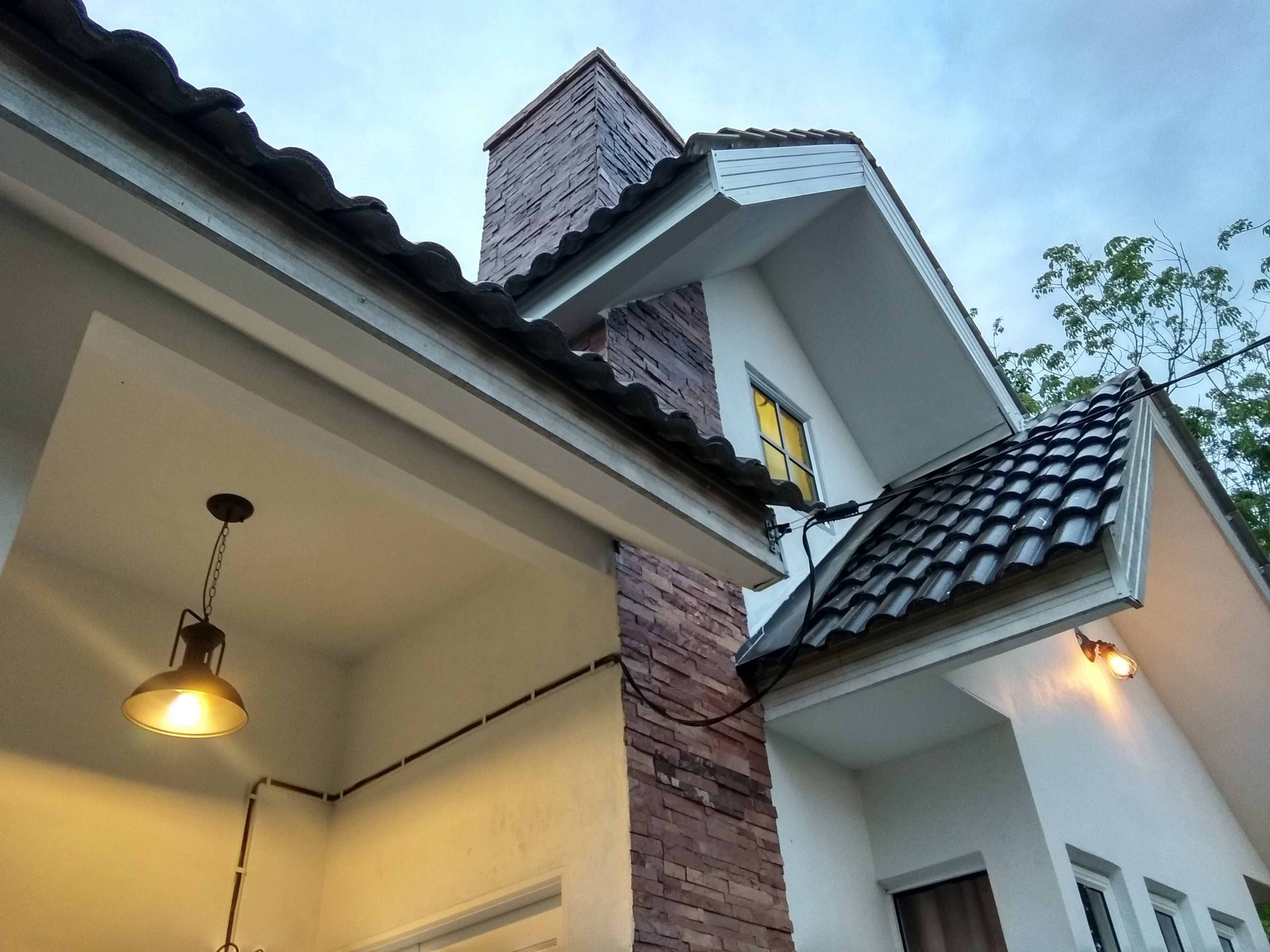 A corner of a building with a brick chimney, a white wall, and a tiled roof.