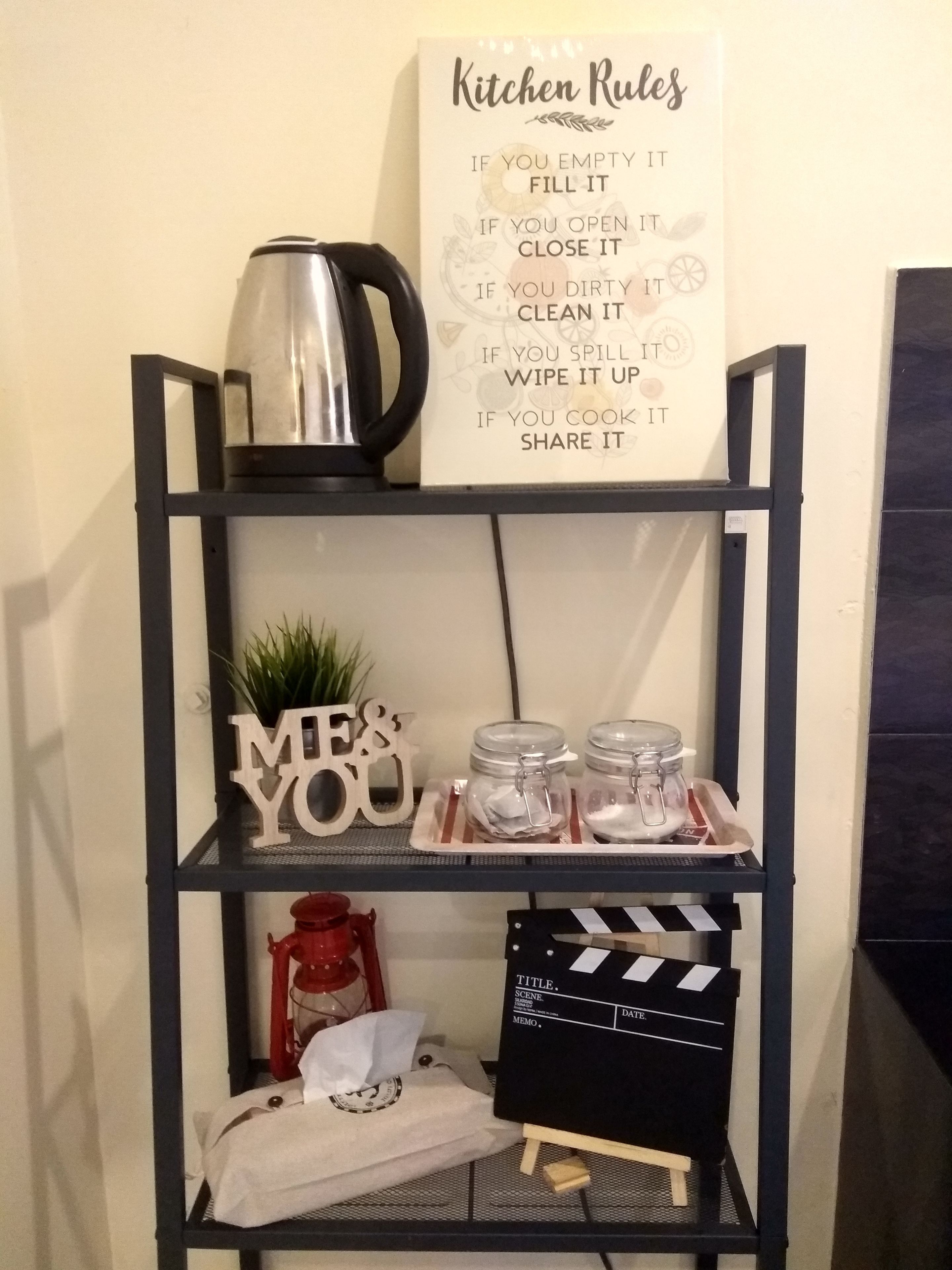 A kitchen shelf with a sign titled "Kitchen Rules," jars, a coffee maker, and a clapperboard.