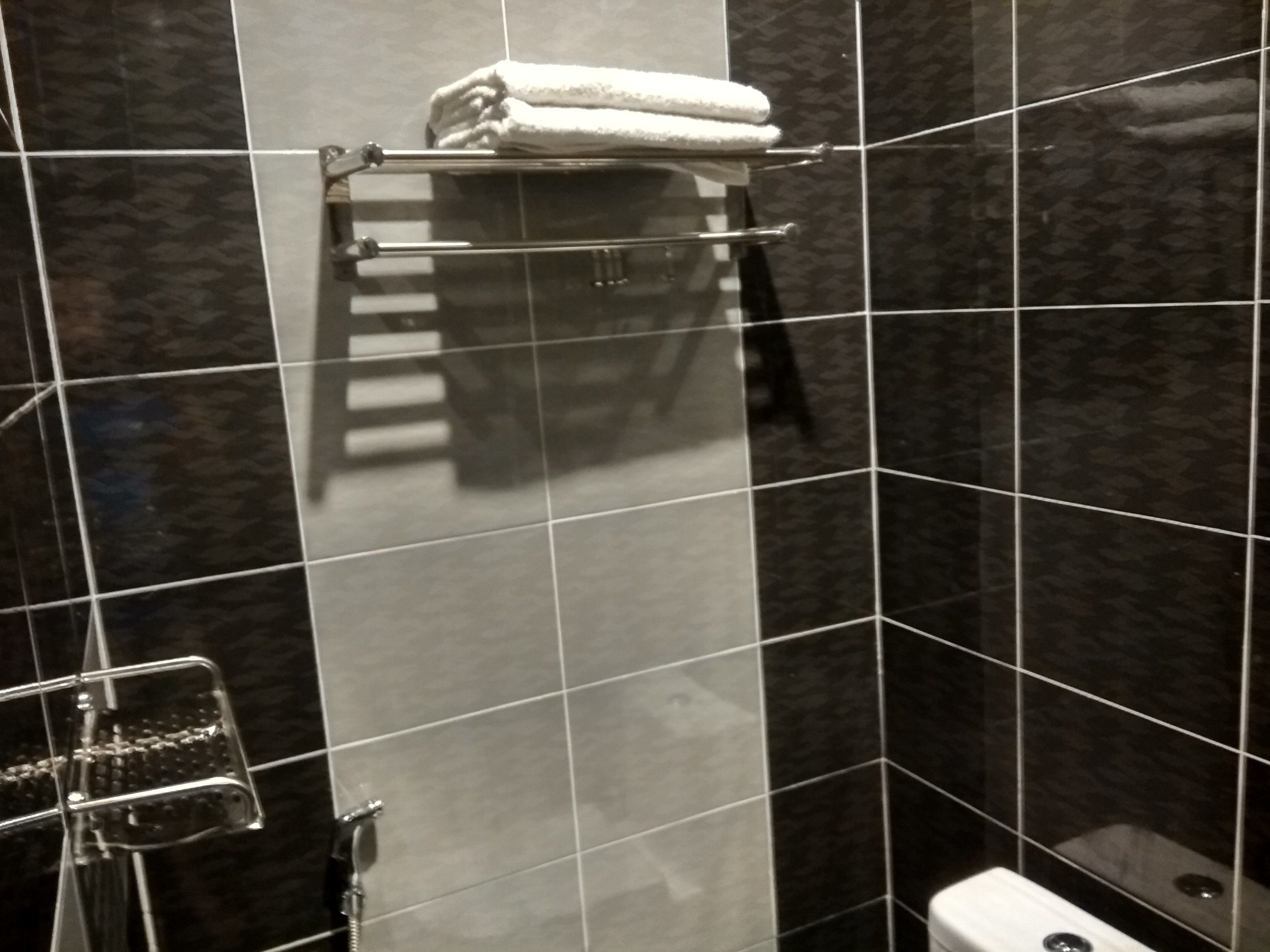 Un baño con baldosas oscuras, un inodoro, una ducha con puerta de cristal y un perchero con una toalla doblada.