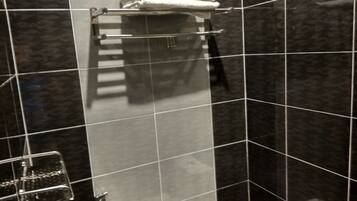 Un baño con baldosas oscuras, un inodoro, una ducha con puerta de cristal y un perchero con una toalla doblada.