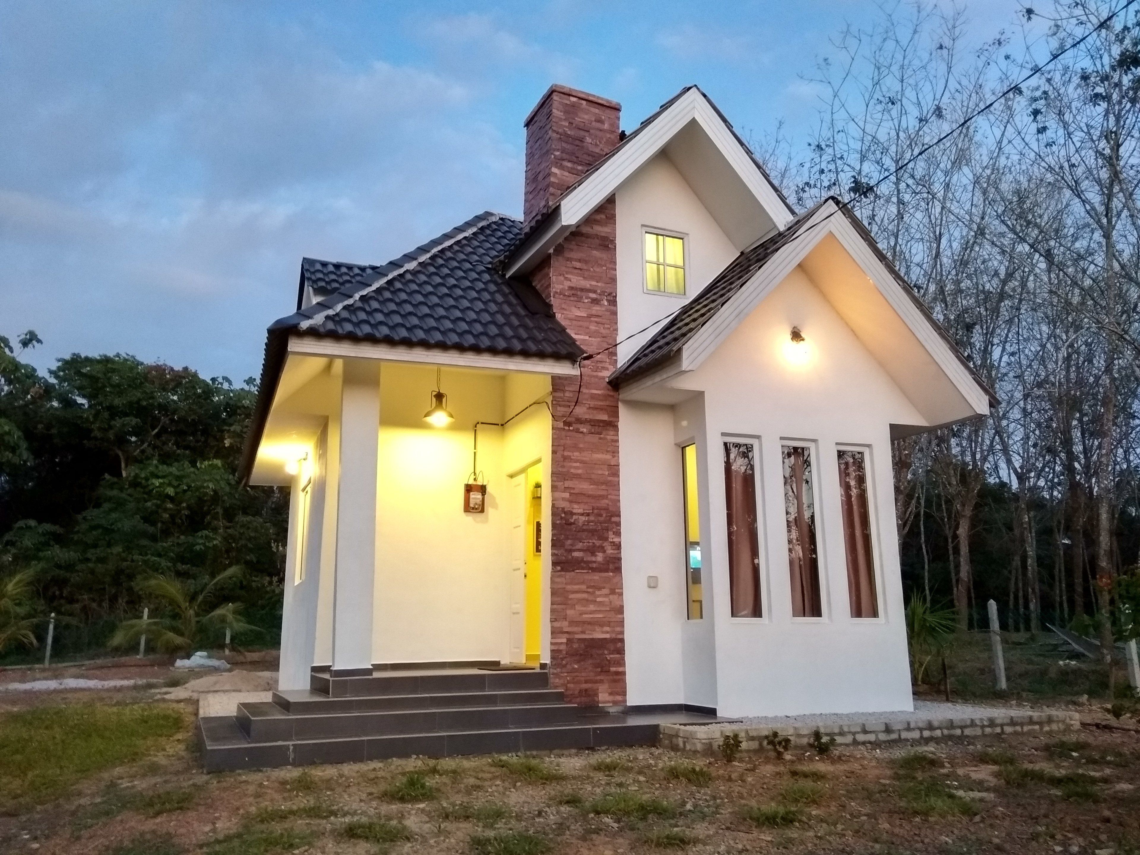 A modern house with a two-story design, featuring a prominent brick chimney, a balcony with a railing, and a well-lit entrance.