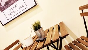 A wooden table with a potted plant, a mug, and a remote control. A framed picture of a farmhouse is on the wall. - Tehel Farmhouse (Jasin)
