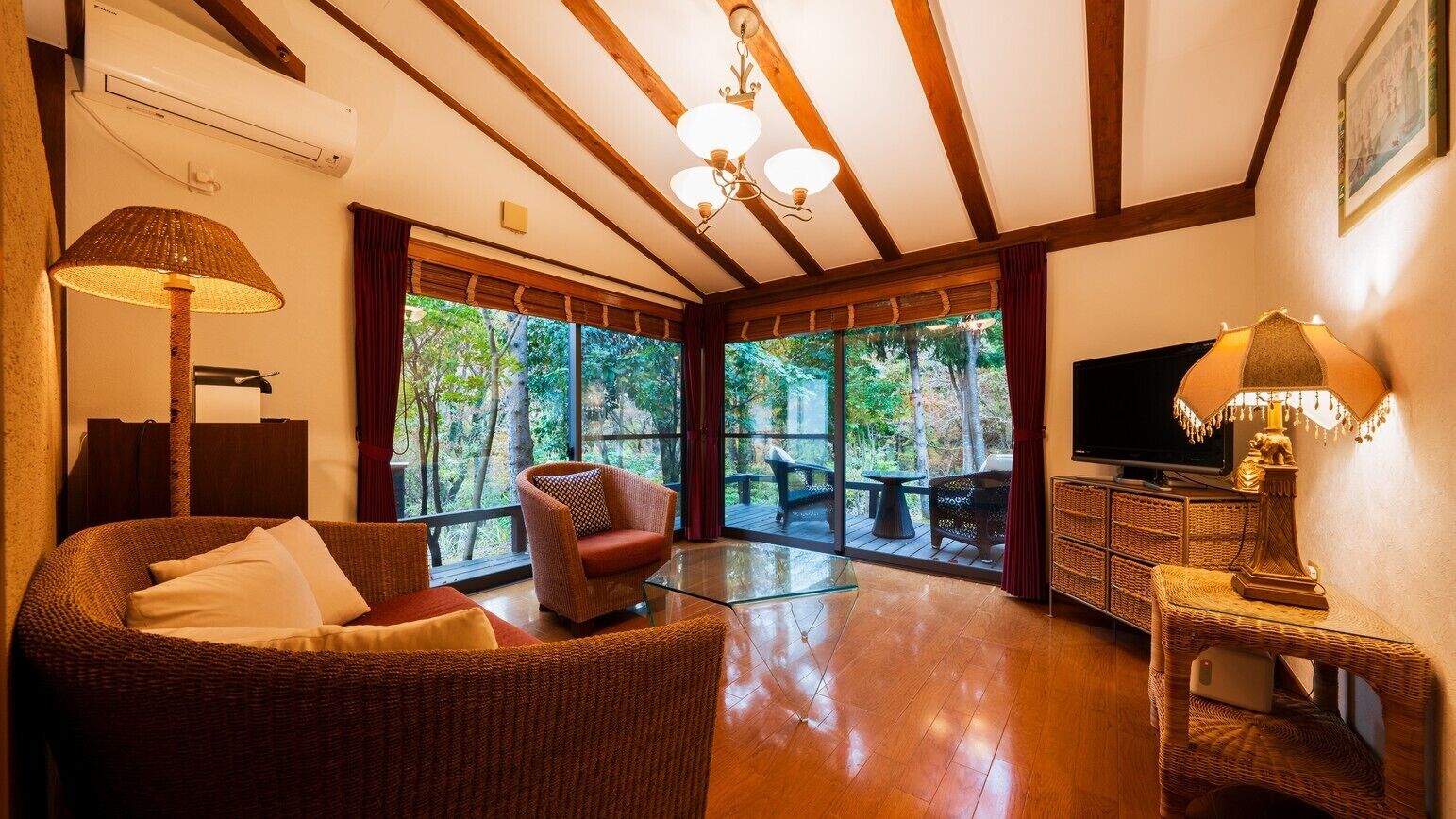 A spacious room with a large window, a television, wicker furniture, and a ceiling fan.