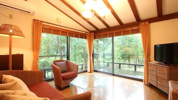 Uma sala de estar ampla com uma janela grande, televisão, móveis de vime e uma mesa de centro de vidro.