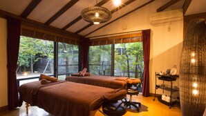 Una habitación con dos camillas de masaje, una lámpara de mimbre y un estante con artículos de aseo.