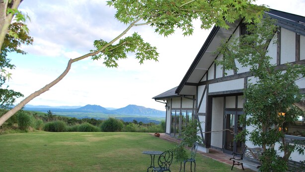 Una casa moderna con un amplio jardín, un comedor con sillas y vistas a montañas.