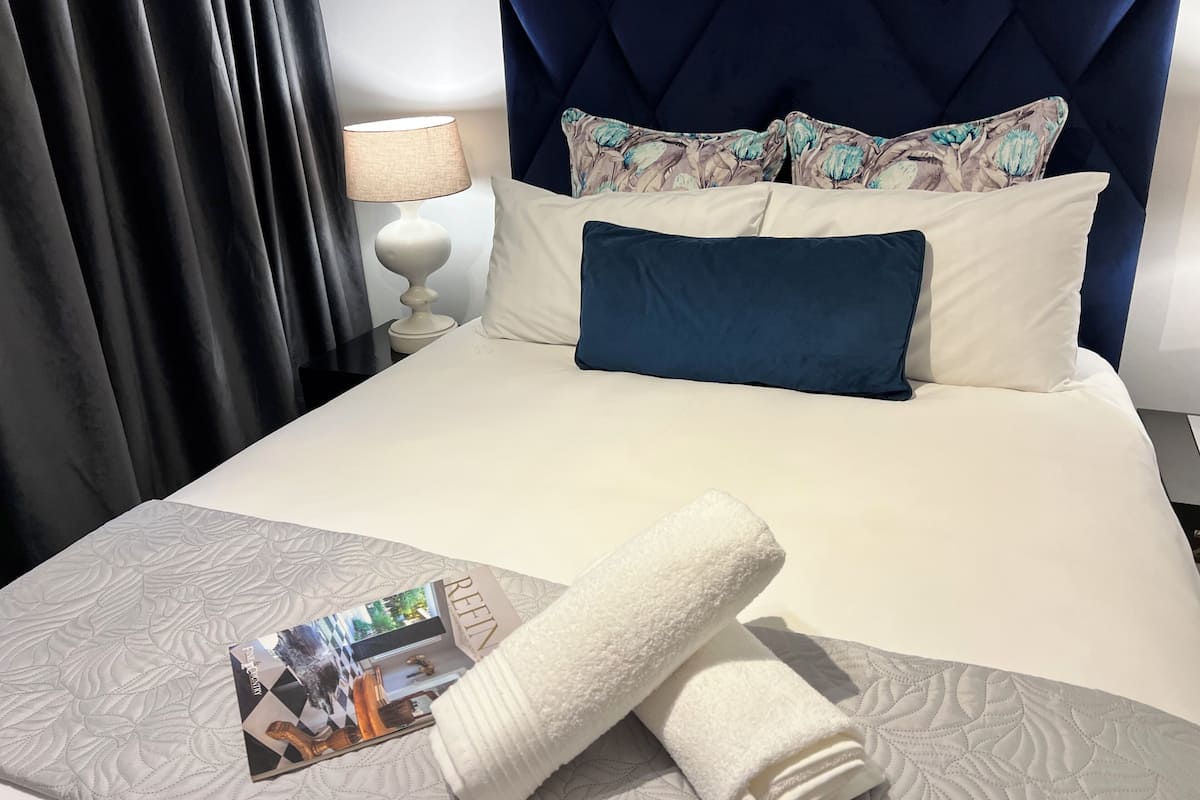 A neatly made bed with a white duvet, a blue pillow, and a folded white towel.