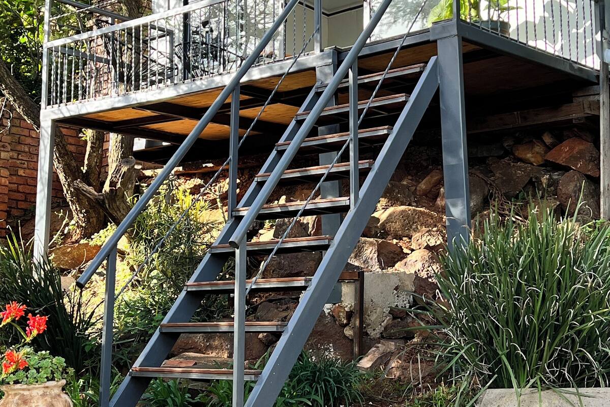 A modern building with a balcony, a staircase leading to an upper level, and surrounding greenery.