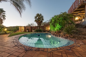 Relax by the pool surrounded by lush greenery and a stone wall.