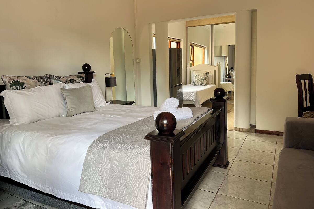 A hotel room with a large bed, a bedside table with a lamp, a mirror, and a chair.