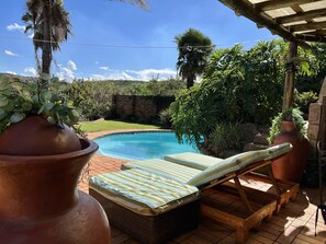 Relax by the serene pool surrounded by lush greenery and a shaded wooden deck.