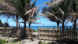 Une clôture en bois mène à une plage bordée de palmiers, d’où l’on a une vue dégagée sur l’océan.