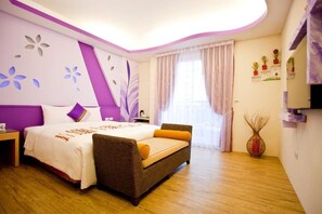 A bedroom with a bed, a sofa, a nightstand, a wall-mounted TV, a window with curtains, and a wall with flower shelves.