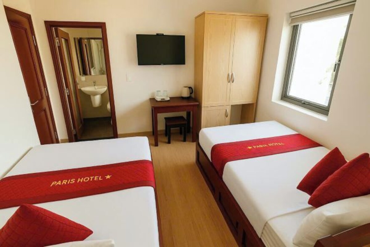 Une chambre d’hôtel avec deux lits, une télévision, une armoire, un lavabo et une fenêtre.