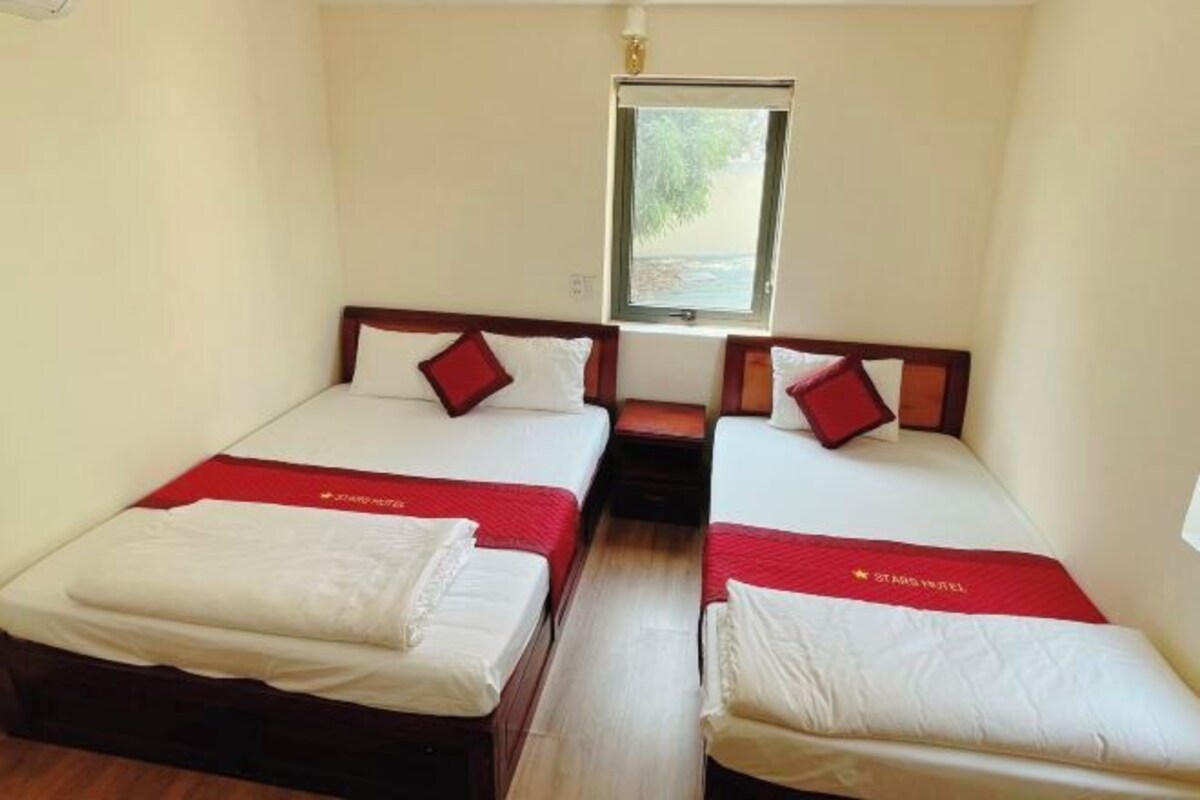 Une chambre avec deux lits, chacun recouvert d’une couverture rouge et agrémenté d’oreillers blancs. Une fenêtre se trouve au-dessus des lits, et une petite table est placée entre eux.