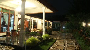 A well-lit outdoor area with a stone pathway, columns, and a covered seating area with a table and chairs.