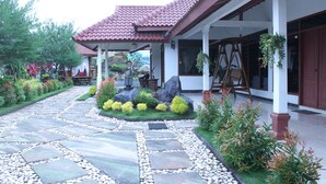 A stone pathway leading to a house with a tiled roof, surrounded by well-maintained gardens and a wooden swing set.