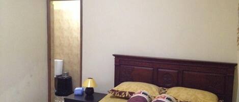 Una habitación de hotel con cama, mesita de noche, lámpara y espejo.