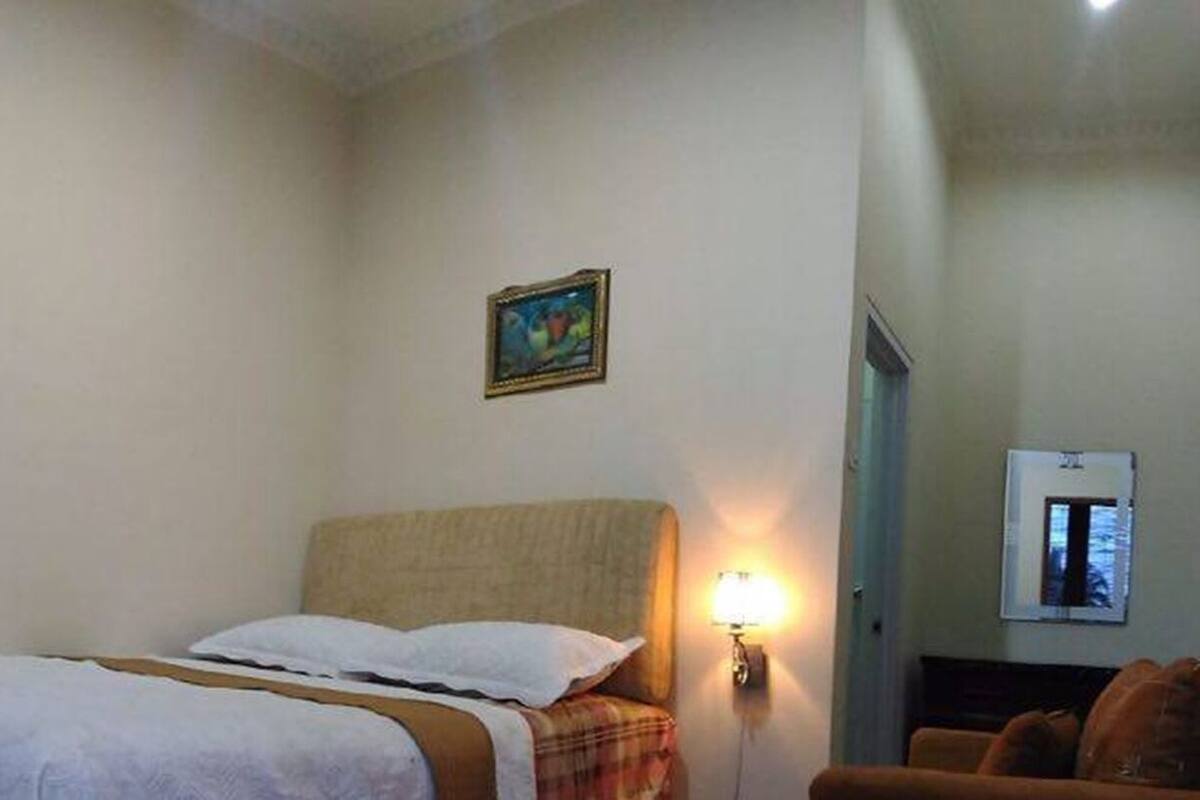 Una habitación de hotel con una cama, televisión montada en la pared, un cuadro y una lámpara.