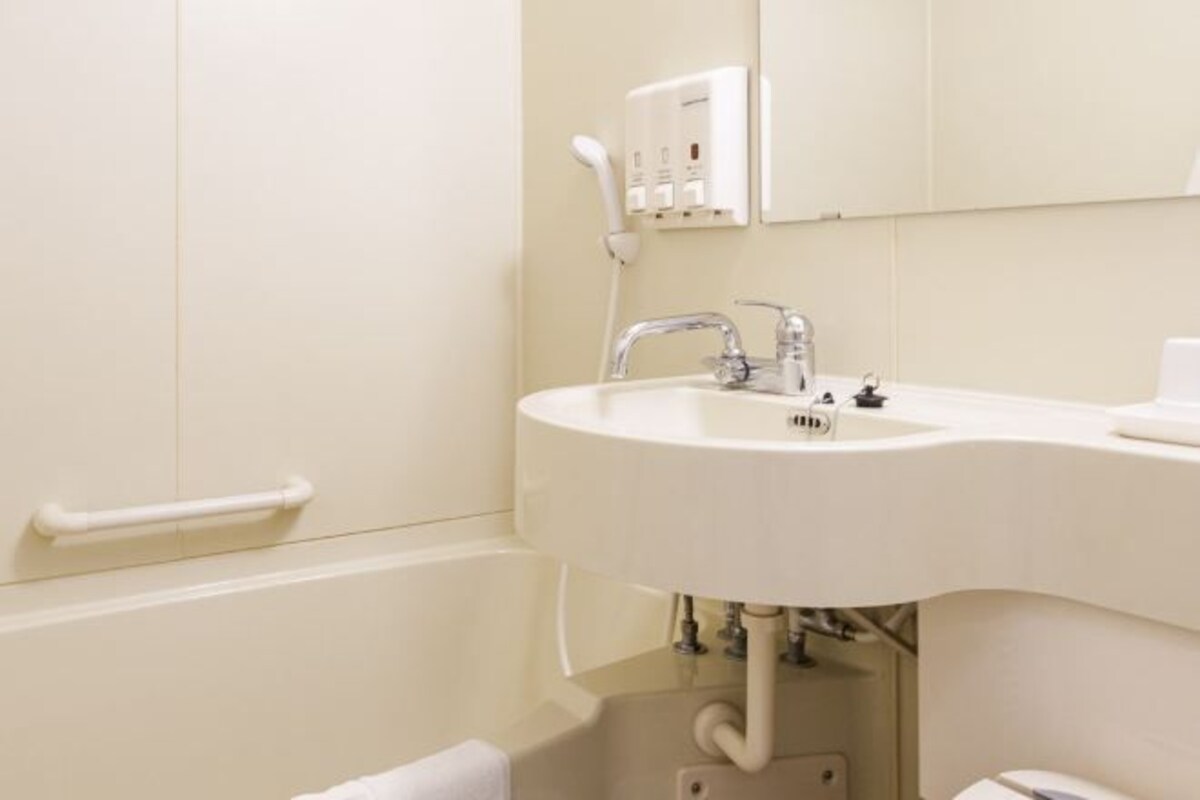 A bathroom with a white sink, a mirror, and a handrail.