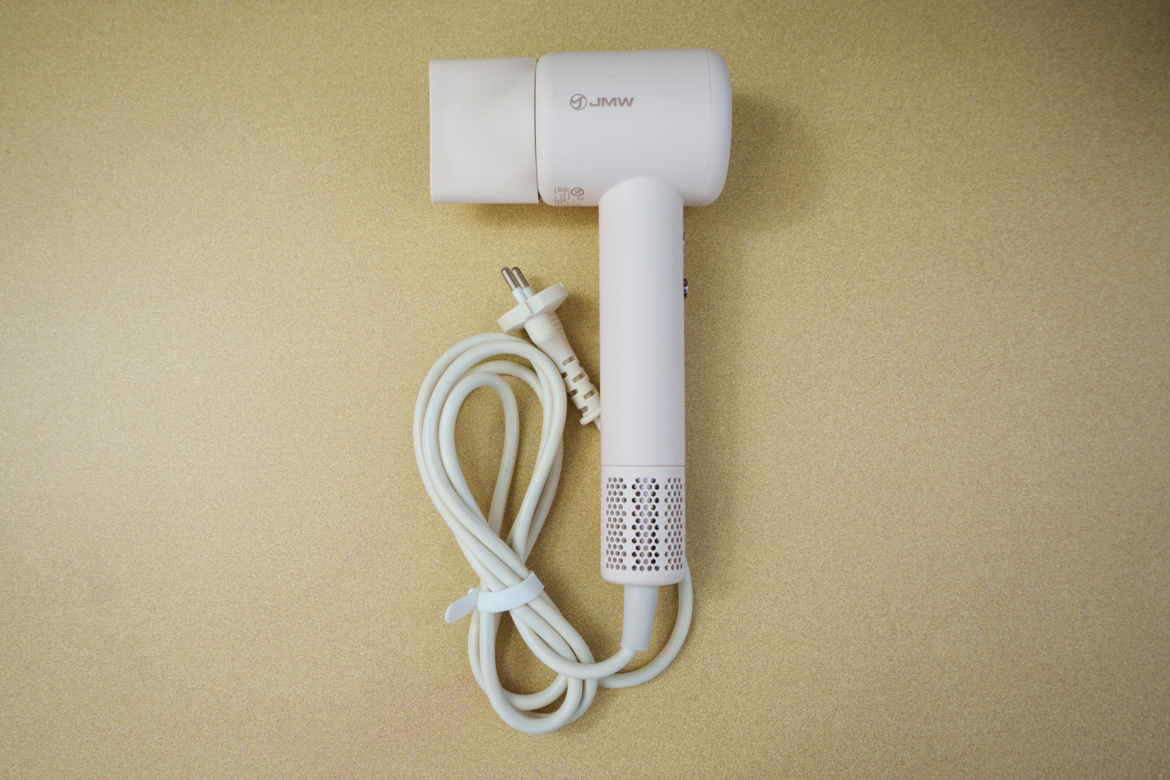 A white cylindrical device with a cable and a plug, placed on a textured surface.