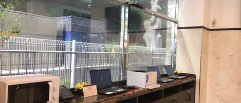 A reception desk with a microwave, two laptops, a telephone, and a vase of flowers.