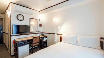 Habitación de hotel con cama, escritorio, silla, televisor, reloj y lámpara de noche.