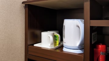 Una kitchenette con una cafetera, una taza blanca y una caja verde sobre una bandeja.