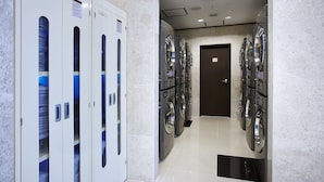 A hotel laundry room with multiple washing machines and dryers, a tiled floor, and a door leading to another area. - Toyoko Inn Incheon Bupyeong (Incheon)