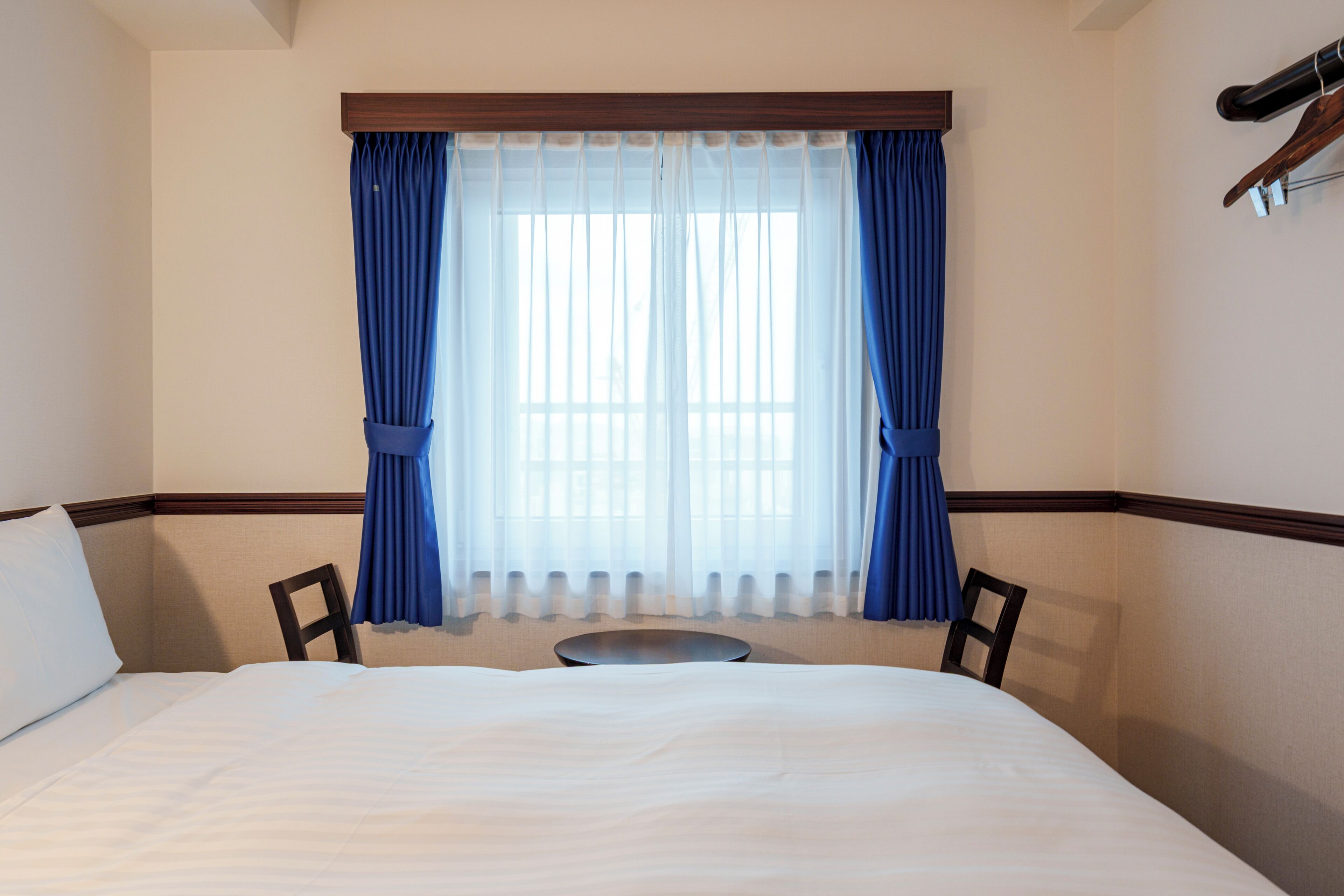 A hotel room with a bed, two chairs, a small table, and a window with curtains.