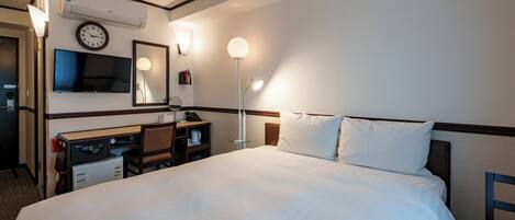 A hotel room with a bed, desk, chair, TV, and wall-mounted clock.