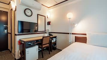 A hotel room with a bed, desk, chair, refrigerator, microwave, clock, and bedside lamp.
