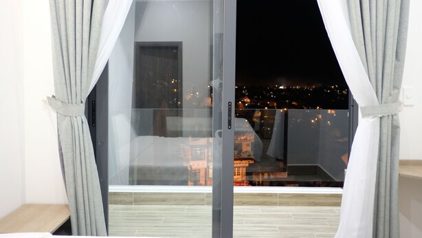 A room with a sliding glass door leading to a balcony with a city view at night. - Dalat Memory Inn (Xuan Huong - Da Lat)