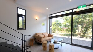 Un interior moderno con una escalera, un sofá beige, una mesa de centro y un ventanal con vistas a zonas verdes.