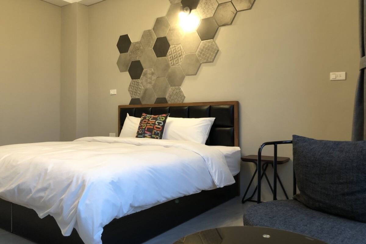 Habitació d'hotel amb un llit, una cadira i una làmpada hexagonal penjada a la paret.